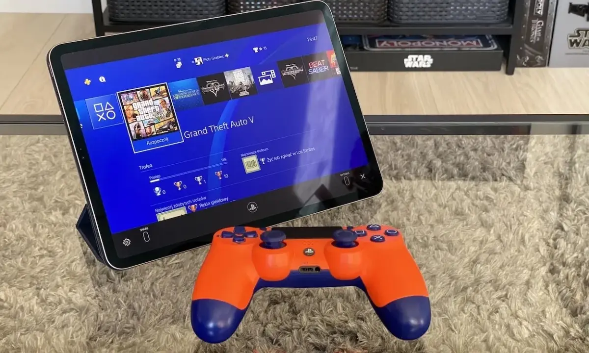Tablet z interfejsem PS4, na którym widać grę GTA V, obok pomarańczowy kontroler. To jakby ps4 emulator pc na wyciągnięcie ręki.