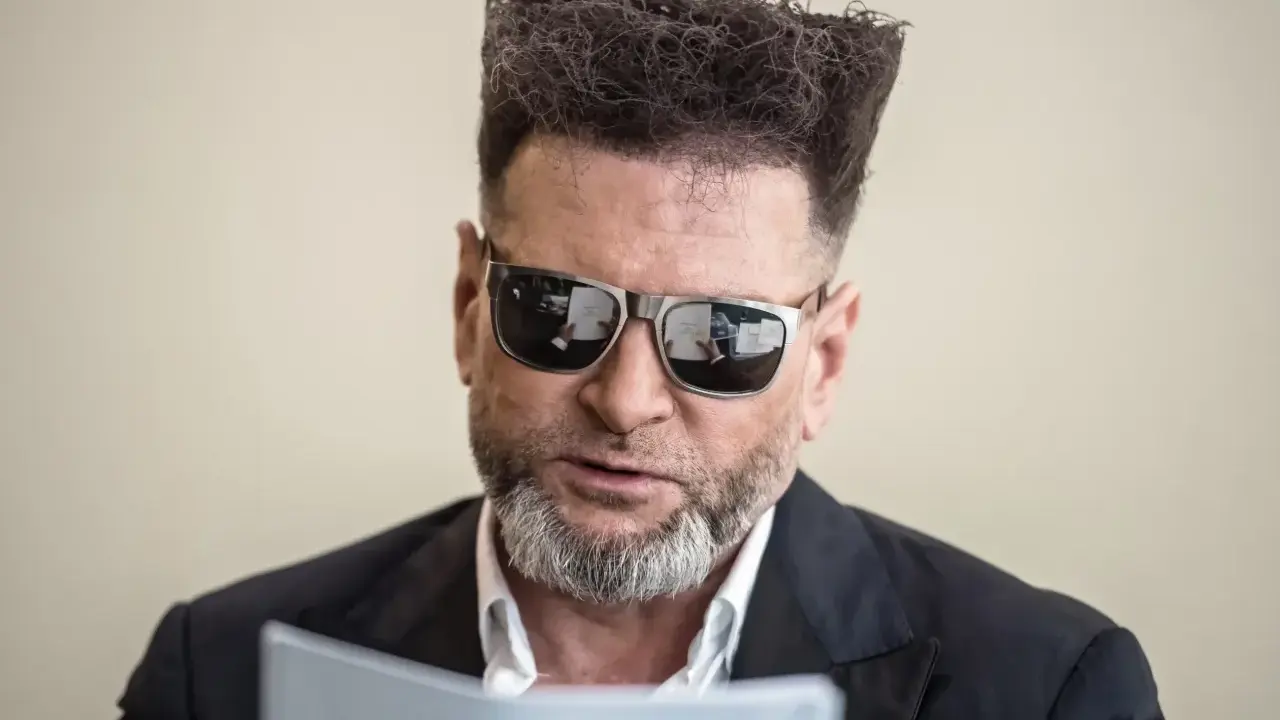 Detektyw Rutkowski is back! Z charakterystyczną fryzurą i okularami, czyta dokumenty.