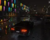 Nocna jazda w GTA 5 z ray tracingiem. Deszcz odbija kolorowe światła neonów od budynku na mokrej ulicy.