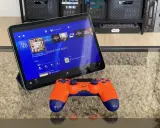 Tablet z interfejsem PS4, na którym widać grę GTA V, obok pomarańczowy kontroler. To jakby ps4 emulator pc na wyciągnięcie ręki.