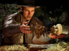 Indiana Jones i wielki krąg: archeolog w kapeluszu i skórzanej kurtce trzyma złoty artefakt w kształcie skarabeusza i skórzaną sakiewkę.