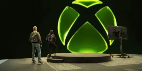 Osoby stoją przed wielkim zielonym logo Xbox. Czy to zapowiedź nowej gry, czy może Xsolla co to za platforma?