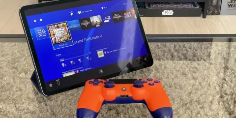 Tablet z interfejsem PS4, na którym widać grę GTA V, obok pomarańczowy kontroler. To jakby ps4 emulator pc na wyciągnięcie ręki.