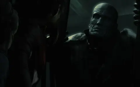 Potworna twarz Nemesisa z Resident Evil w mroku, groźnie spogląda na Claire.