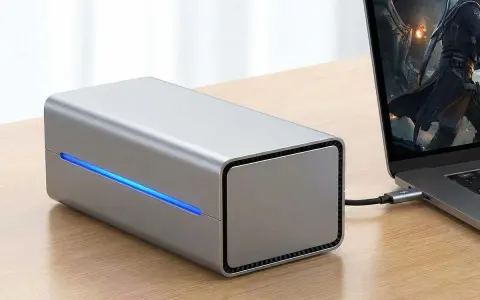 Srebrna obudowa egpu do laptopa z niebieskim podświetleniem, podłączona do laptopa z grą na ekranie.