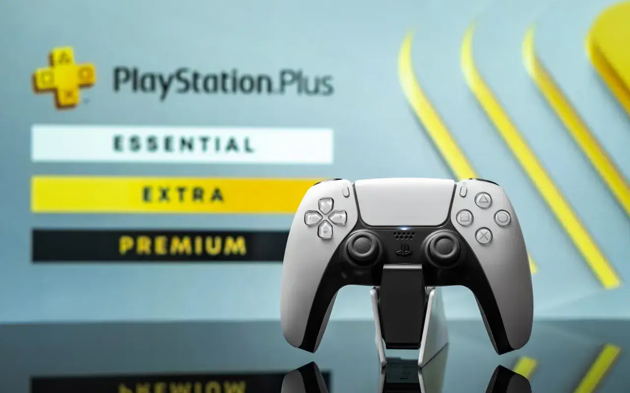 Biały kontroler DualSense na tle menu PlayStation Plus z opcjami Essential, Extra i Premium.