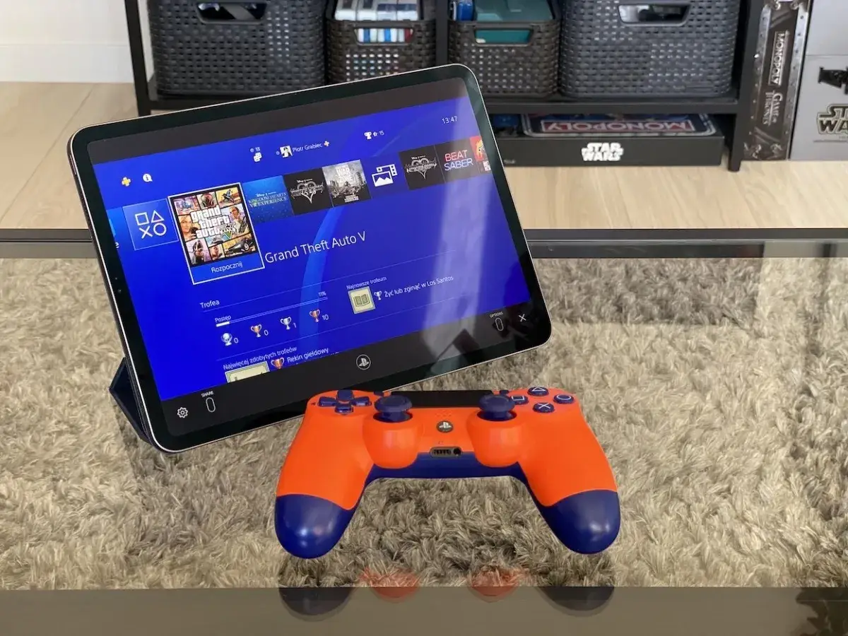 Tablet z interfejsem PS4, na którym widać grę GTA V, obok pomarańczowy kontroler. To jakby ps4 emulator pc na wyciągnięcie ręki.