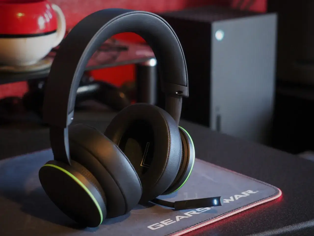 Słuchawki bezprzewodowe na podkładce z logo Gears of War, obok konsoli Xbox Series X. Dowiedz się, jak podłączyć słuchawki bezprzewodowe do Xbox Series X.