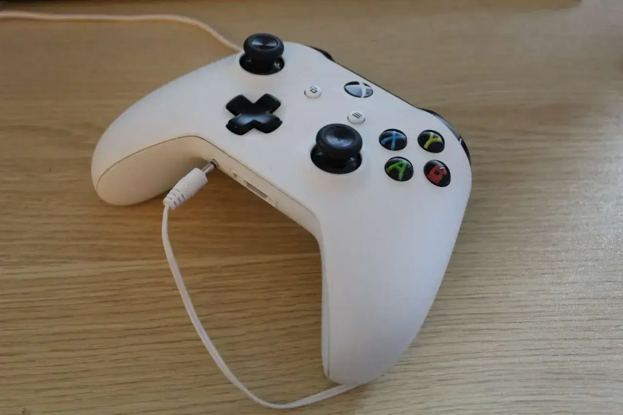 Biały kontroler Xbox z podłączonymi słuchawkami. Prosty sposób, jak podłączyć słuchawki do Xboxa, by cieszyć się dźwiękiem.