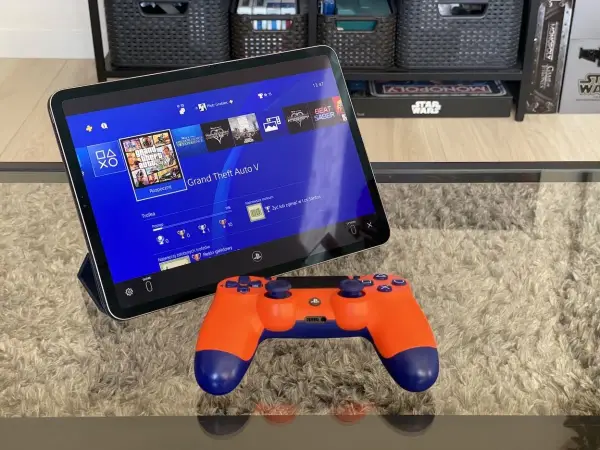 Tablet z interfejsem PS4, na którym widać grę GTA V, obok pomarańczowy kontroler. To jakby ps4 emulator pc na wyciągnięcie ręki.