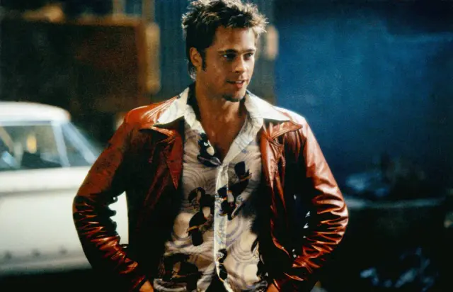 Brad Pitt w skórzanej kurtce i wzorzystej koszuli, z rękami w kieszeniach, wygląda na gotowego do akcji.